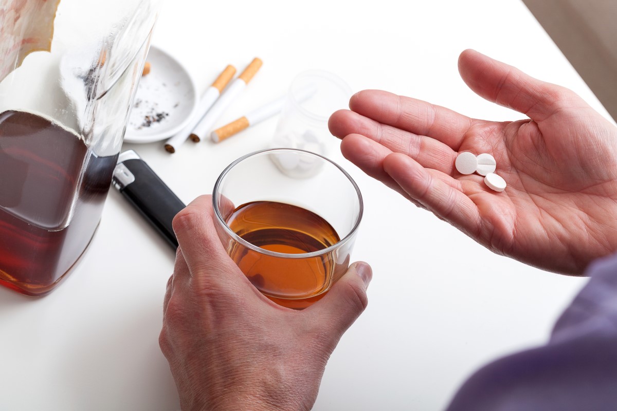 Alkohol, fajčenie a lieky. Človek drží pohár hnedého alkoholu a lieky v pravej ruke. Ako najčastejšie príčiny chronickej pankreatitídy