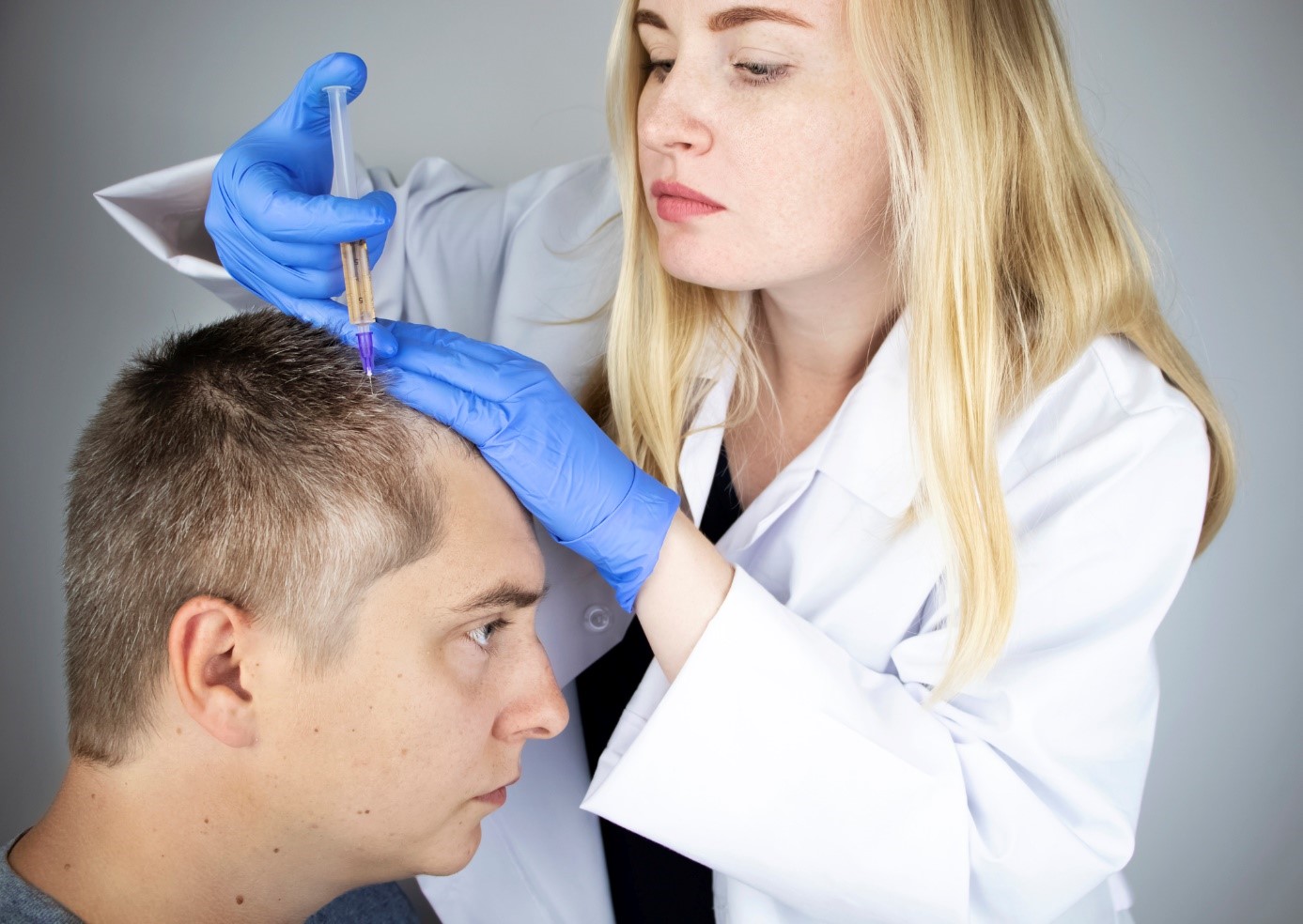 Liečba vypadávania vlasov, lekárka dávkuje injekčne liek do hlavy pána, pacienta