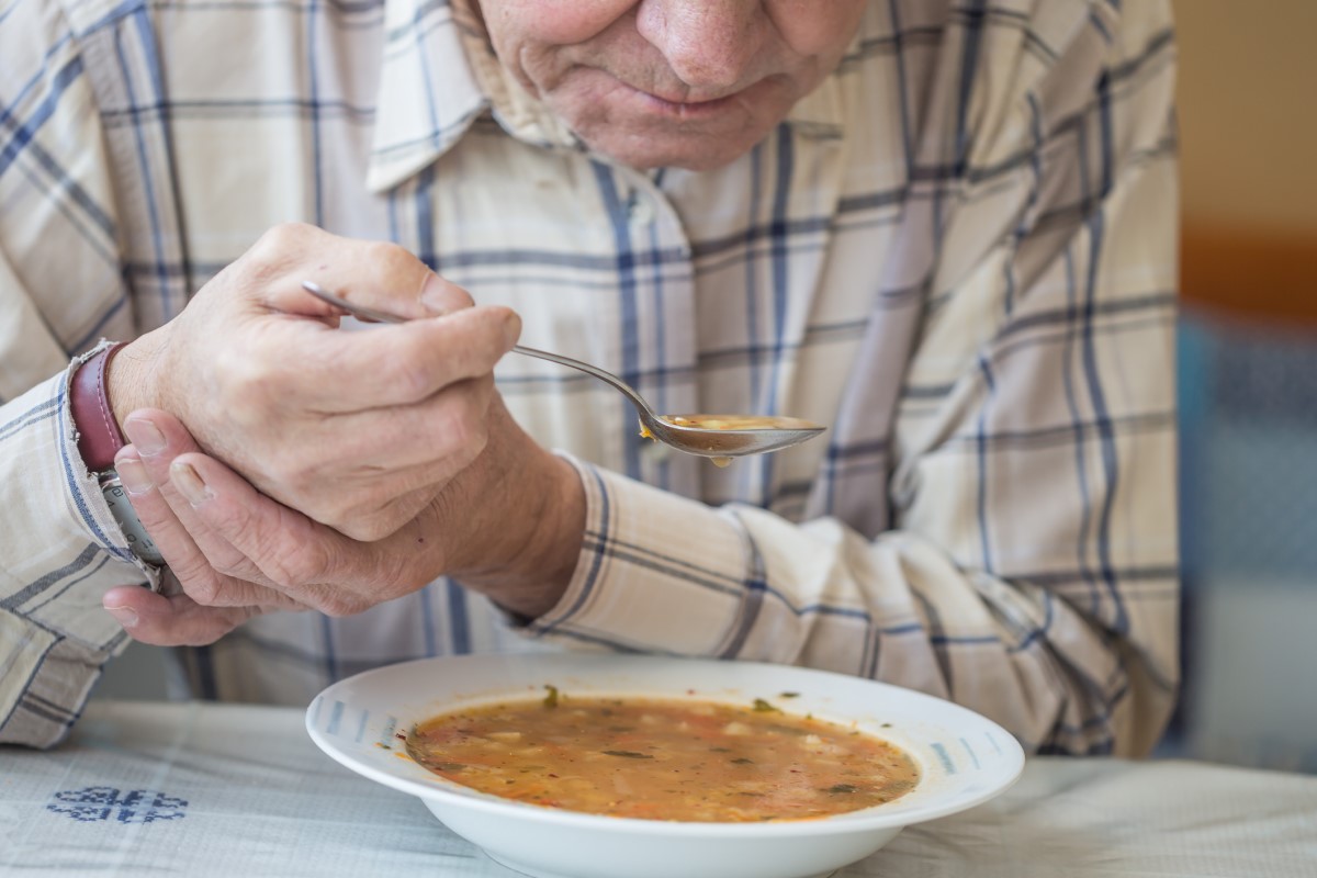 Muž je polievku, pridržiava si ruku pre tras pri Parkinsone