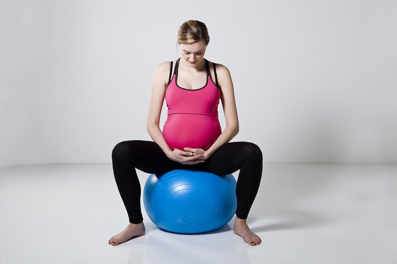 Schwangere Frau, die auf einem fitten Ball sitzt.