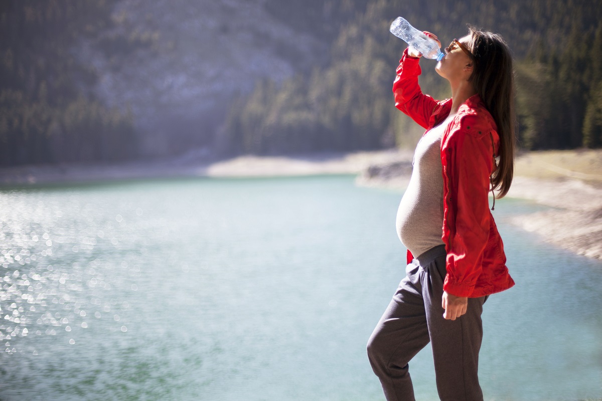 Schwangere Frau, die spazieren geht und Wasser trinkt. 