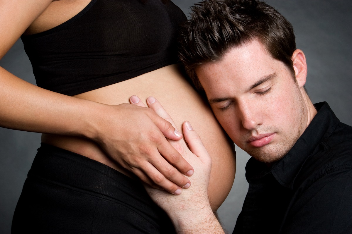 A man with his ear pressed to the belly of a pregnant woman listens to the fetal heartbeat.