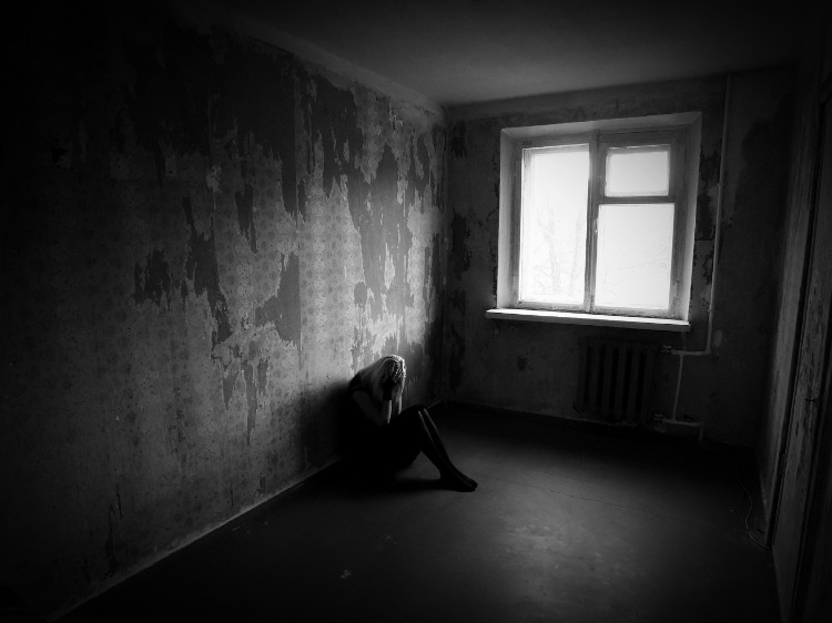 žena sediaca v tmavej miestnosti opretá o stenu a rukami si drží tvár