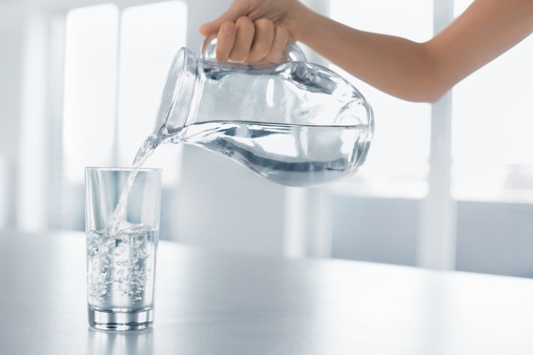 ruka nalievajúca čistú vodu z fľaše do pohára