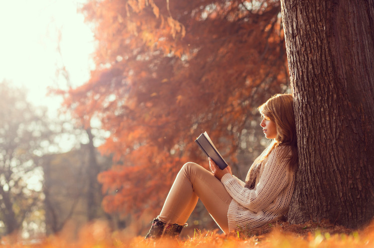 žena sediaca v lese, opretá o strom čita knižku v jesennom období