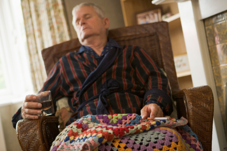 spiaci dedko v kresle prikrytý dekou, v ruke má pohár s alkoholom a cigaretu