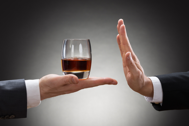 ruka človeka drží pohár s alkoholom a druhá ruka iného človeka ho odmieta
