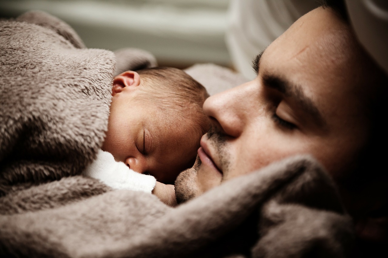 dieťatko spí vedľa otca pod hnedou dekou
