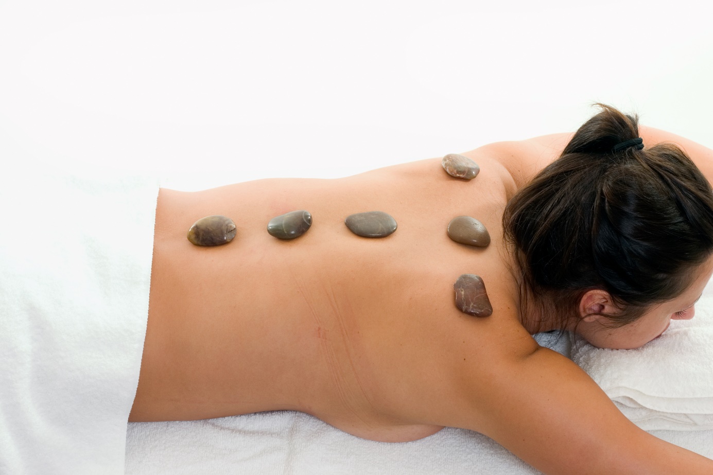 Masážne kamene položené na chrbte ženy, ako súčasť kúpeľnej a masážnej liečby