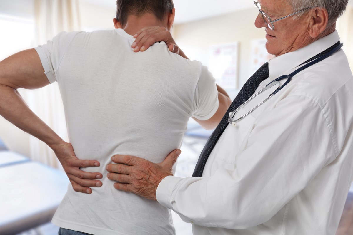 Bolesť chrbta, lekár vyšetruje mladého muža, bolí ho chrbát