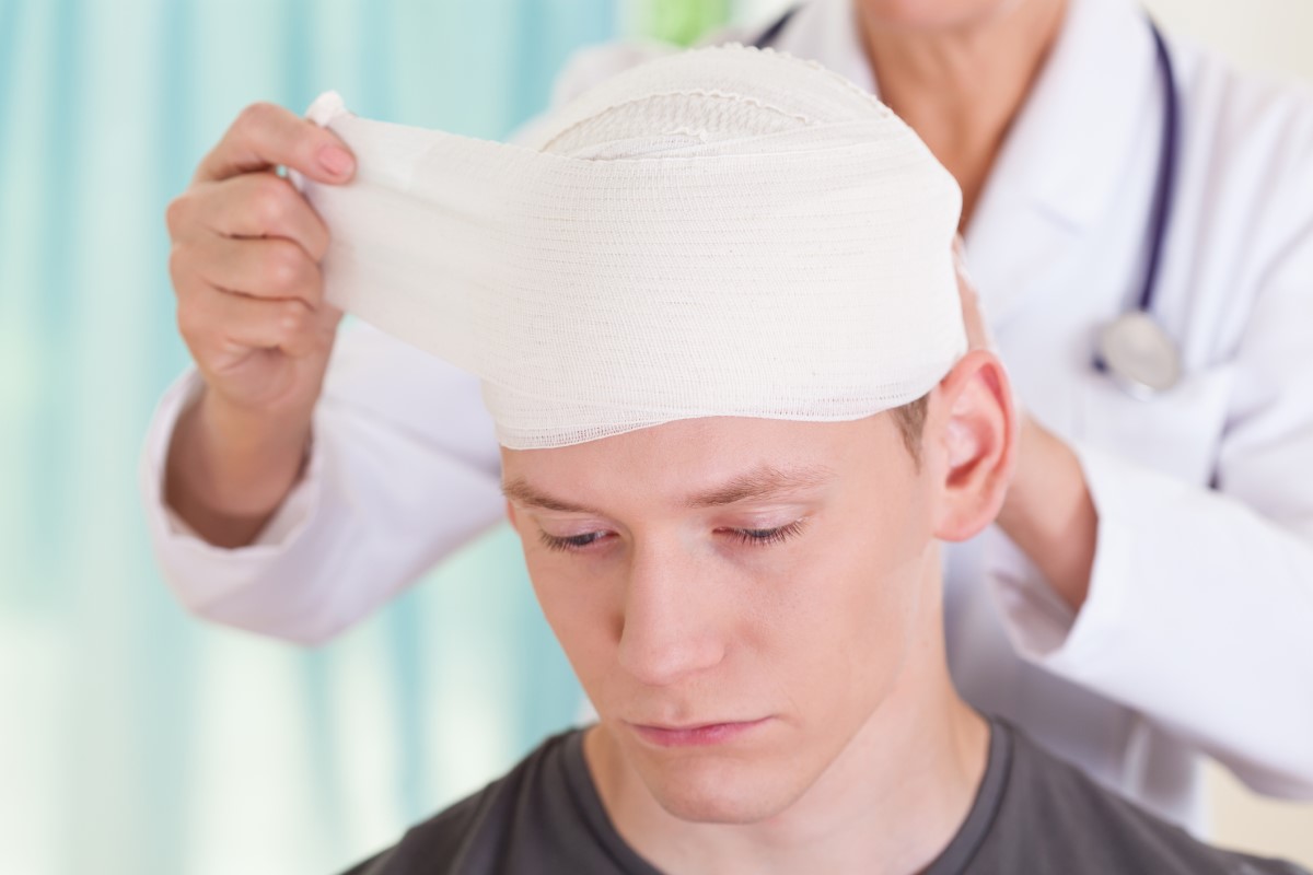 Bolesť hlavy po úraze, obviazaná hlava, lekár ošetruje chlapca s úrazom hlavy
