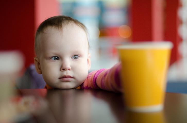 Malé dieťa dočahuje pohár vody na stole
