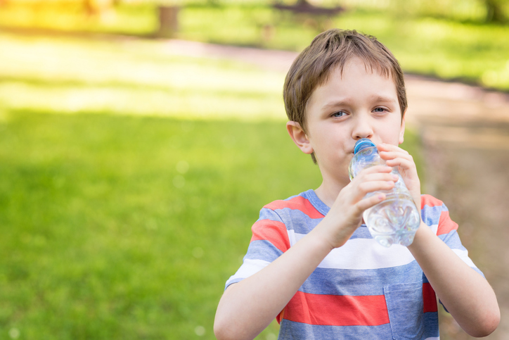 Chlapec pije vodu z fľašky, zelená tráva na pozadí