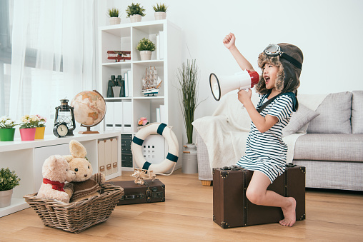 Dievčatko v baranici sedí v obývacej izbe na kufri a drží megafón