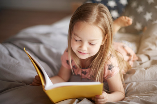 Dievčatko číta žltú knihu na posteli