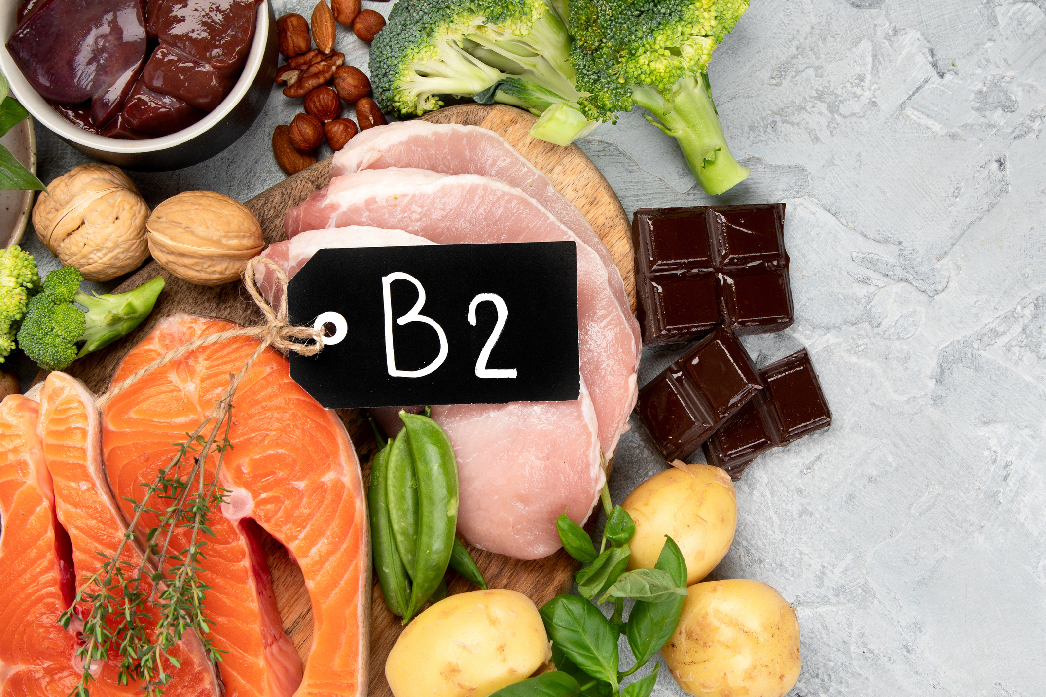 Potraviny s obsahom B2 - orechy, mäso, pečeň, čokoláda, brokolica, losos, hrach ako zdroje vitamínov a štítok s nápisom B2