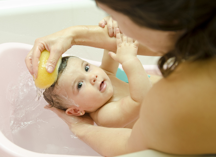 Matka umýva dieťa vo vaničke so špongiou