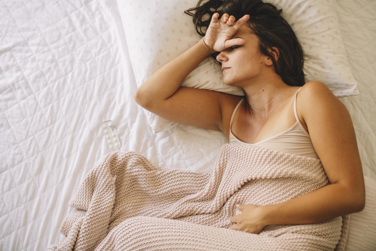 Žena má migrenózne bolesti hlavy, leží v posteli a má zdravotné ťažkosti