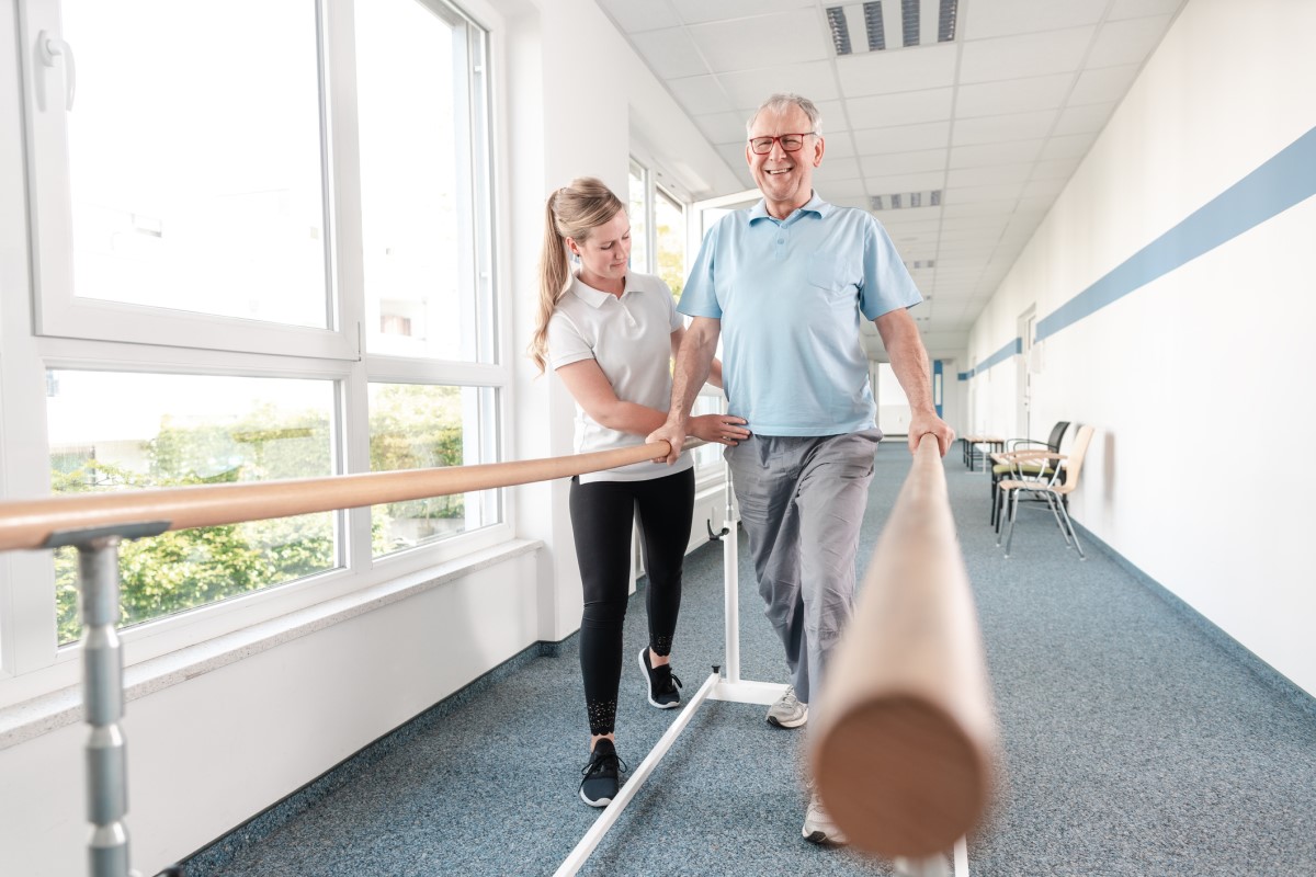 Fyzioterapia s cieľom zvýšenia sebestačnosti, motoriky  a hybnosti pacienta. Senior cvičí - žena zdravotník mu pomáha