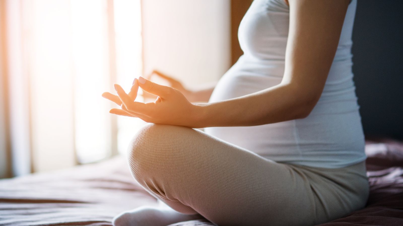 Dychové cvičenia pomáhajú uvoľniť telo a pripraviť sa na pôrod. Zdroj foto: Canva Záber na tehotenské bruško. Žena sedí v relaxačnej pozícii pre dychové a meditačné cvičenia.