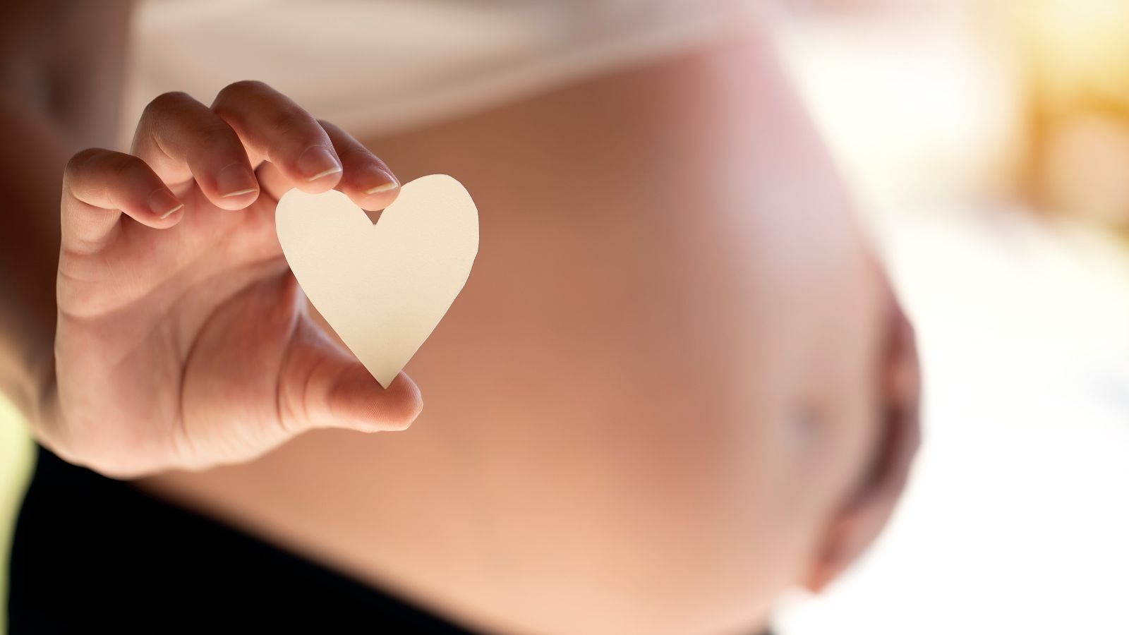 Nečakajte a nesnažte sa o samoliečbu. V tehotenstve je nutné odborné vyšetrenie, ktoré je prevenciou komplikácií a ohrozenia zdravia bábätka a matky (plodu a tehotnej ženy). Zdroj foto: Canva Žena drží malé srdiečko z papiera v ruke