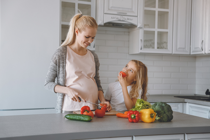 Tehotná matka s dcérou pripravujú zdravé jedlo v kuchyni.