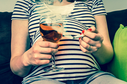 Tehotná žena v pásikavom tričku so zapálenou cigaretou a pohárom vína