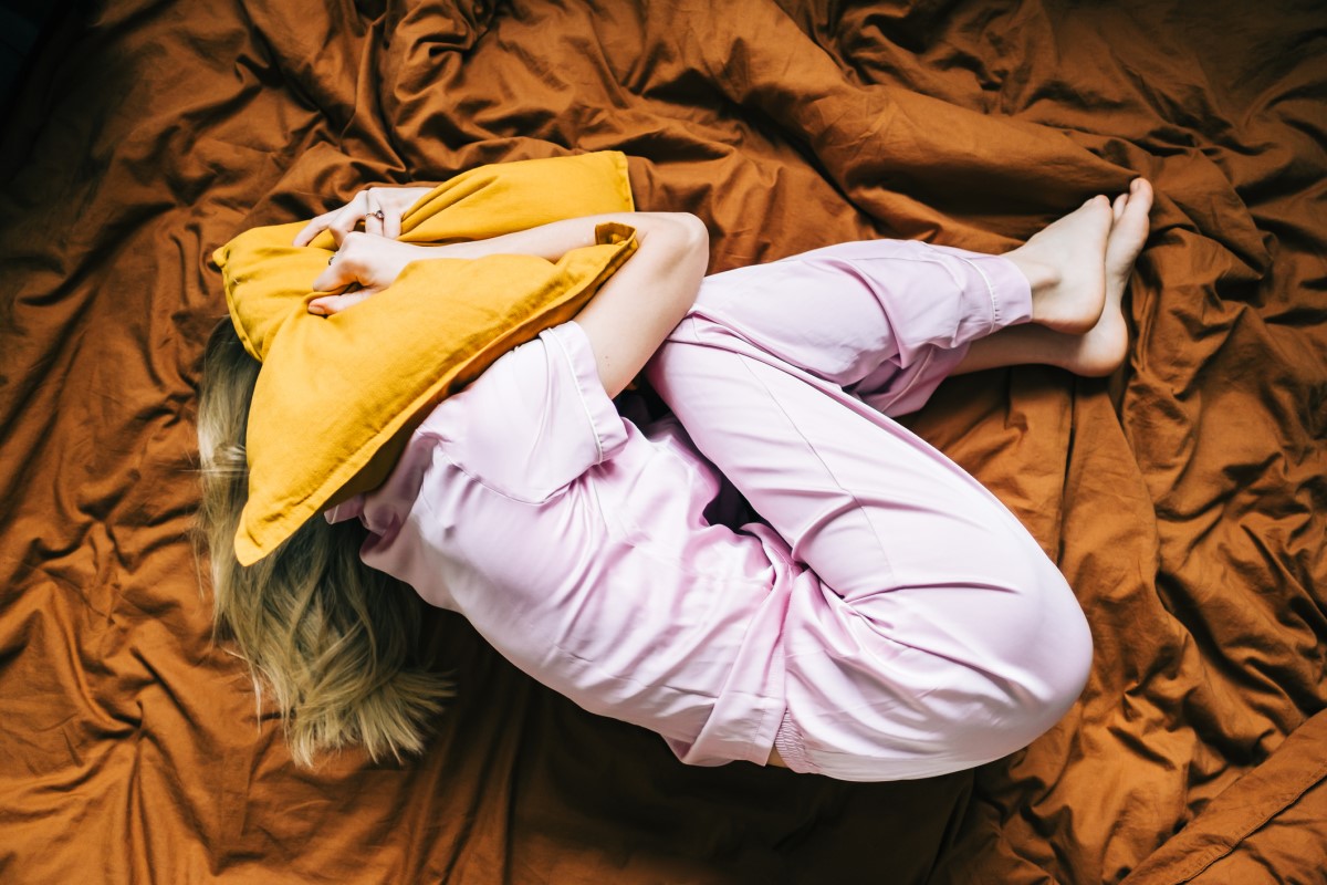 Unavená a ubolená žena leží v posteli, zakrýva si hlavu vankúšom