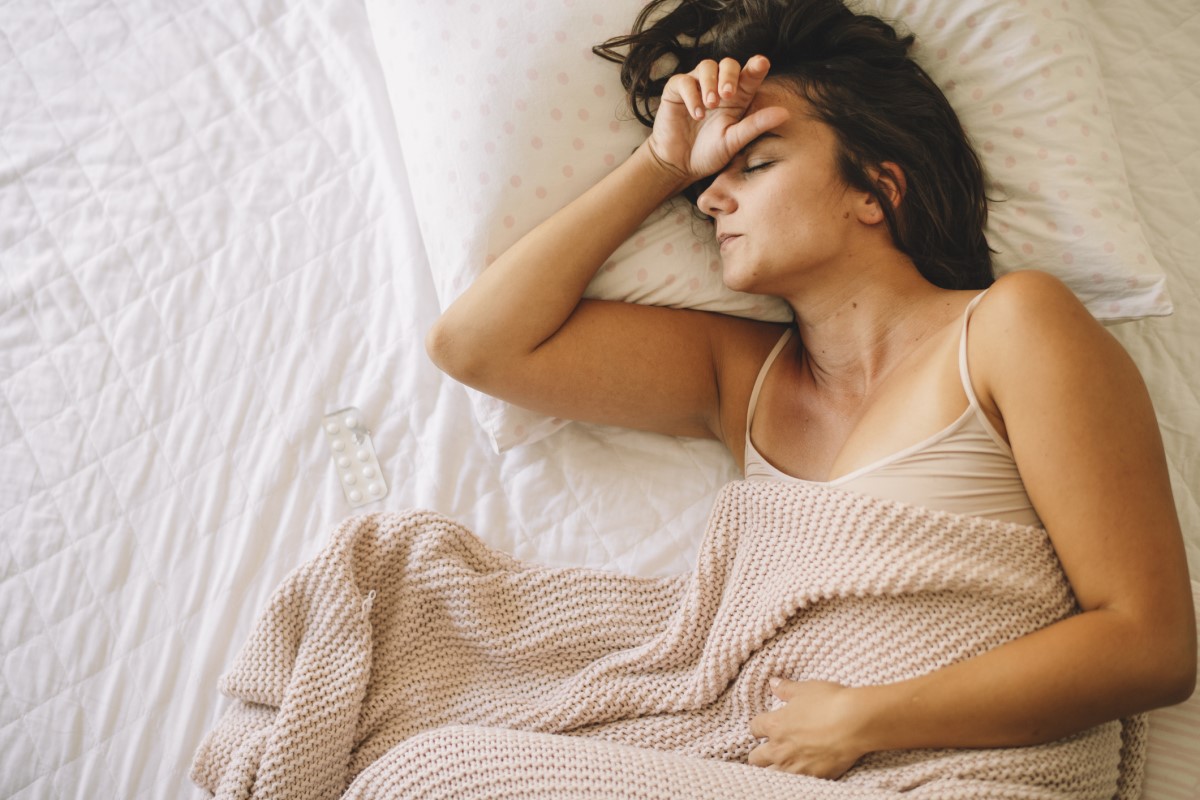 Unavená žena leží v posteli, bolí ju brucho