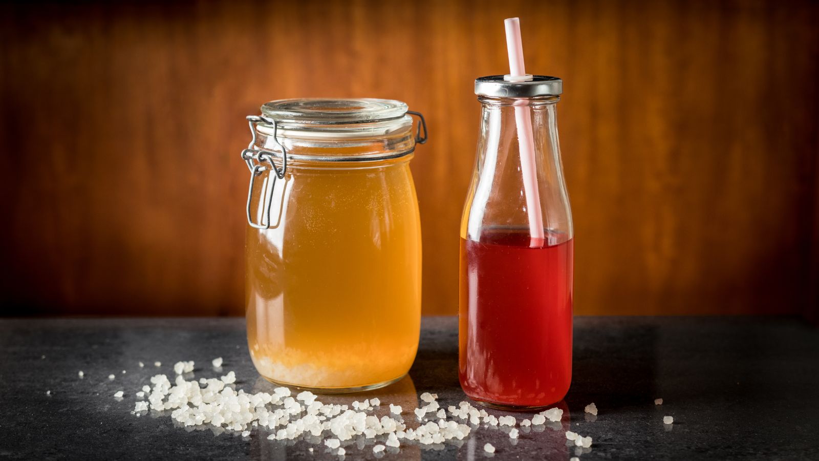 Benefity: jemne sladkokyslá chuť, probiotické kultúry, hydratácia. Zdroj foto: Canva Vodný kefírový probiotický nápoj v pohári a vo fľaške s ovocnými prísadami. Okolo nádob sú kryštáliky vodného kefíru. Domáca výroba.