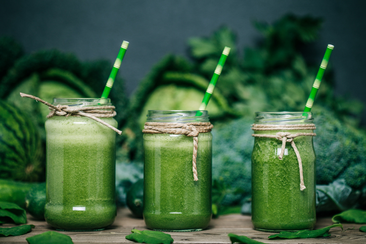 Zelené zeleninové smoothie, tri poháre, v pozadí kapusta, brokolica a hrach