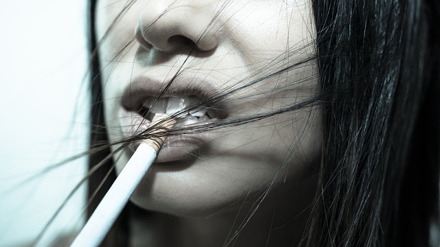 Žena má na pere položenú cigaretu, vlasy jej vejú vo vetre. Fajčenie je rizikom pre chrup