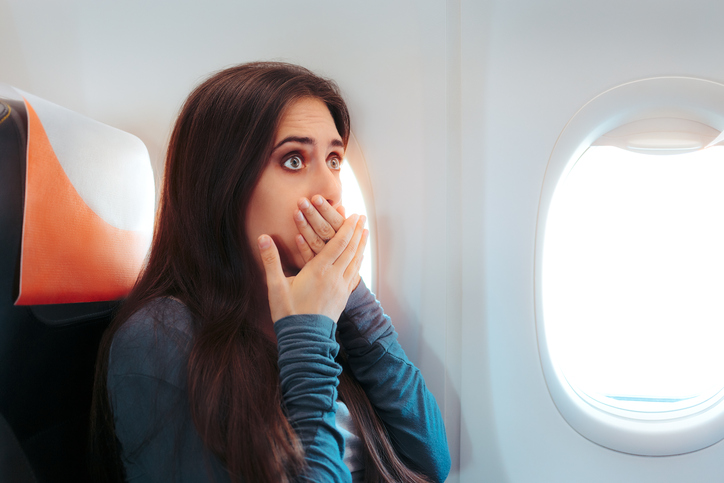 žena sediaca v lietadle pri okne, napína ju na zvracanie