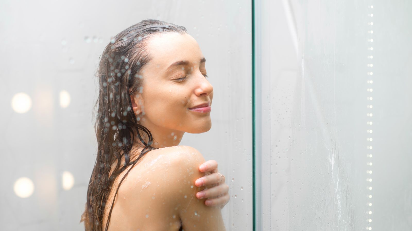 Žena v sprche po opaľovaní. Očista a hydratácia pokožky po opaľovaní. Záber na usmiatu tvár a rameno.
