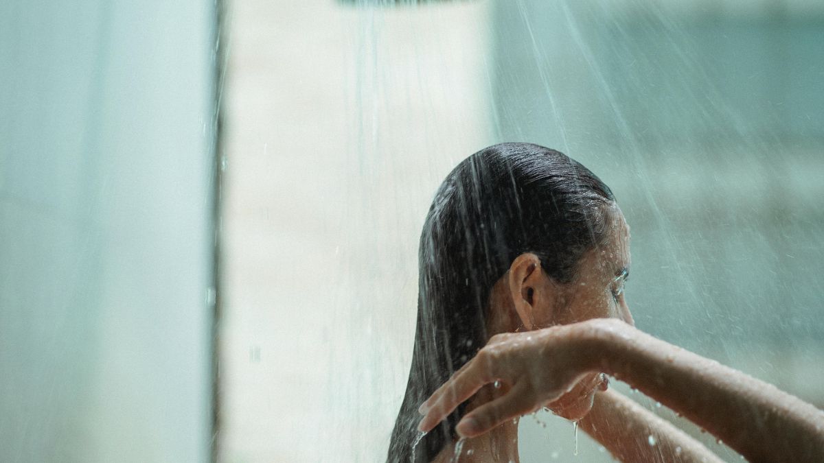 Pri umývaní tela a tváre môžete použiť jemný čistiaci prostriedok alebo sprchový gél určený pre plavcov. Zdroj foto: Canva Žena v sprche, záber po plecia s rukami na vlasoch. Sprchovanie po kúpaní sa v mori alebo v bazéne. Starostlivosť o pokožku tela.