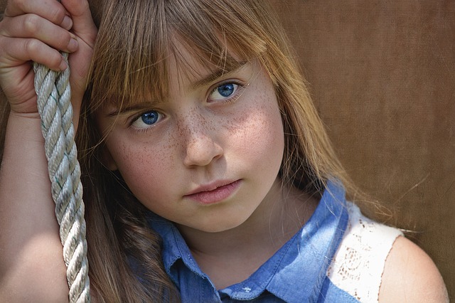 mladé dievča sedí na hojdačke, má neutrálny pohľad, modré oči