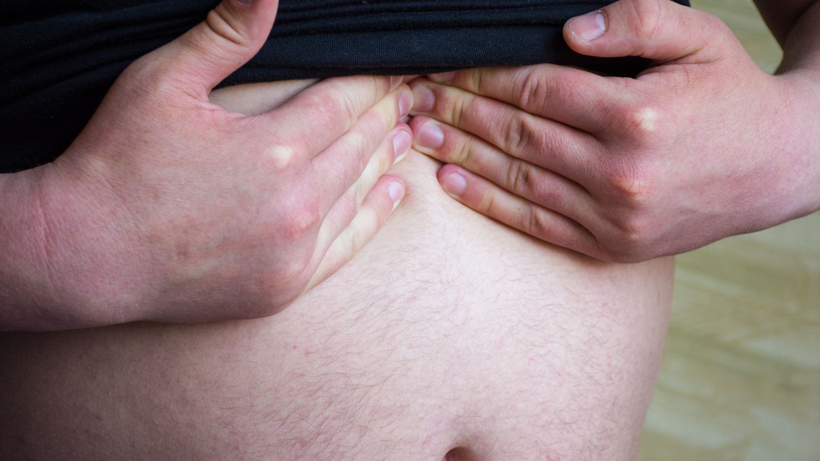 Muž má odhalené brucho a drží si časť epigastria
