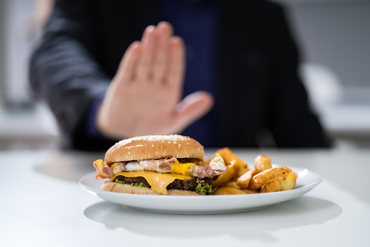 Nevhodné jedlo ako príčina pálenia záhy - hamburger na tanieri, ktorý odmieta muž