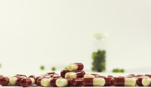 Lieky voľne rosypané, červenobielej farby a v pozadí lieky zelenej farby vo fľaštičke