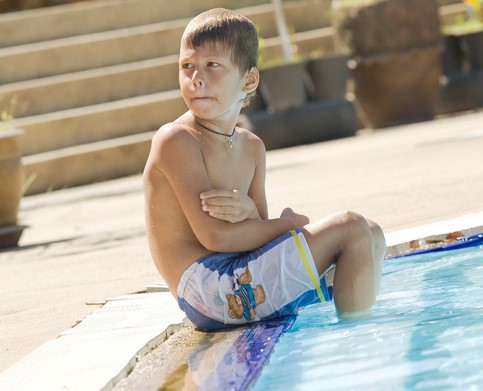 Chlapec sedí pri bazéne, nohy vvo vode je mu zima