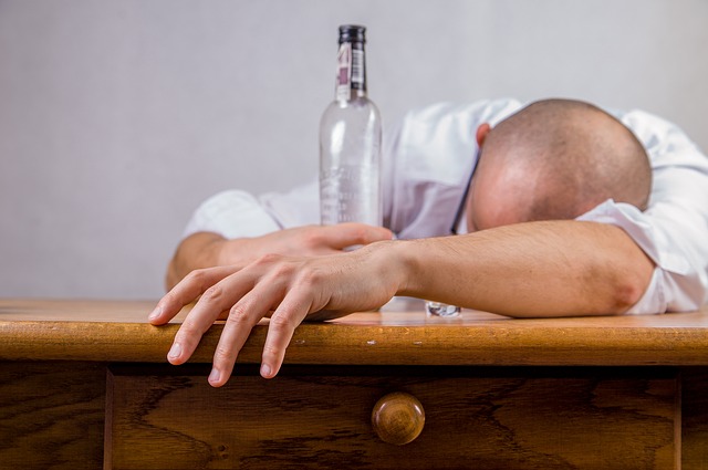 Alkoholizmus je príčinou porúch nálady, muž leží na stole v ruke má prázdnu fľašu alkoholu, alkoholik