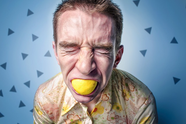 muž s citrónom v ústach má kyslý výraz tváre, možná alergická reakcia na citrus