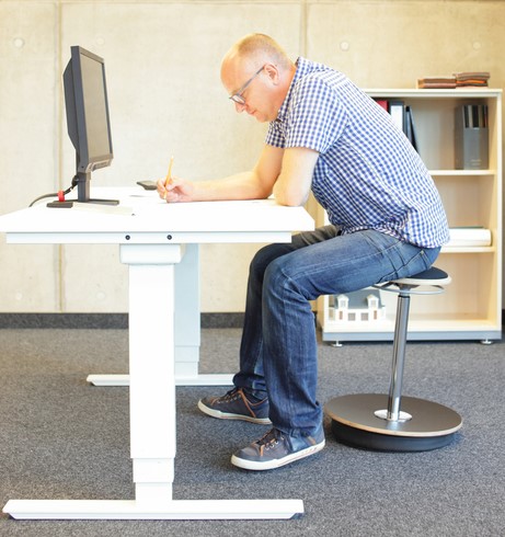 Muž sedí za počítačovým stolom, má sedavé zamestnanie