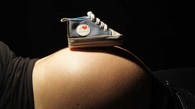 tehotná žena leží, na bruchu má detskú topánočku
